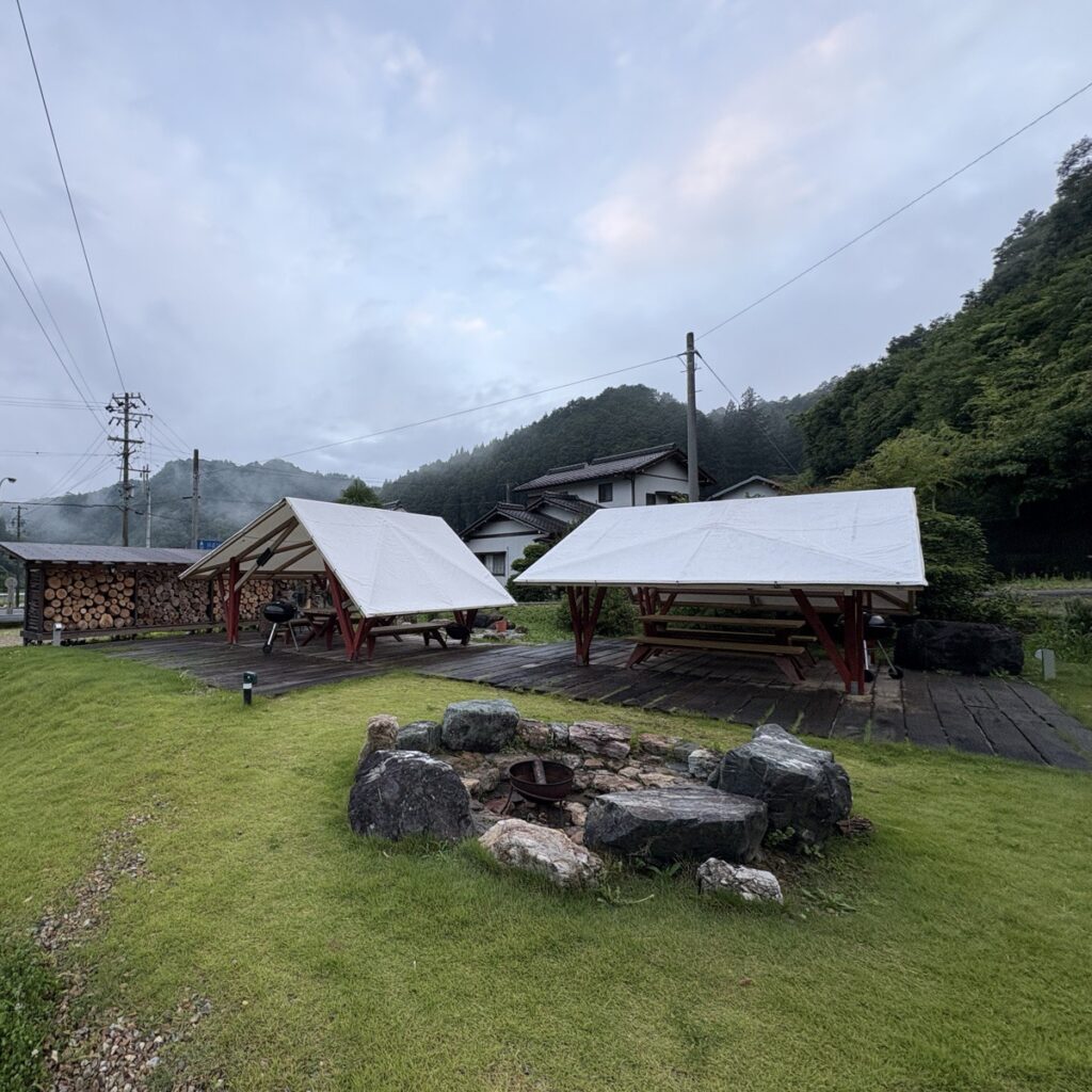 つづやビレッジの敷地。焚き火スペースと薪棚、山あいの集落