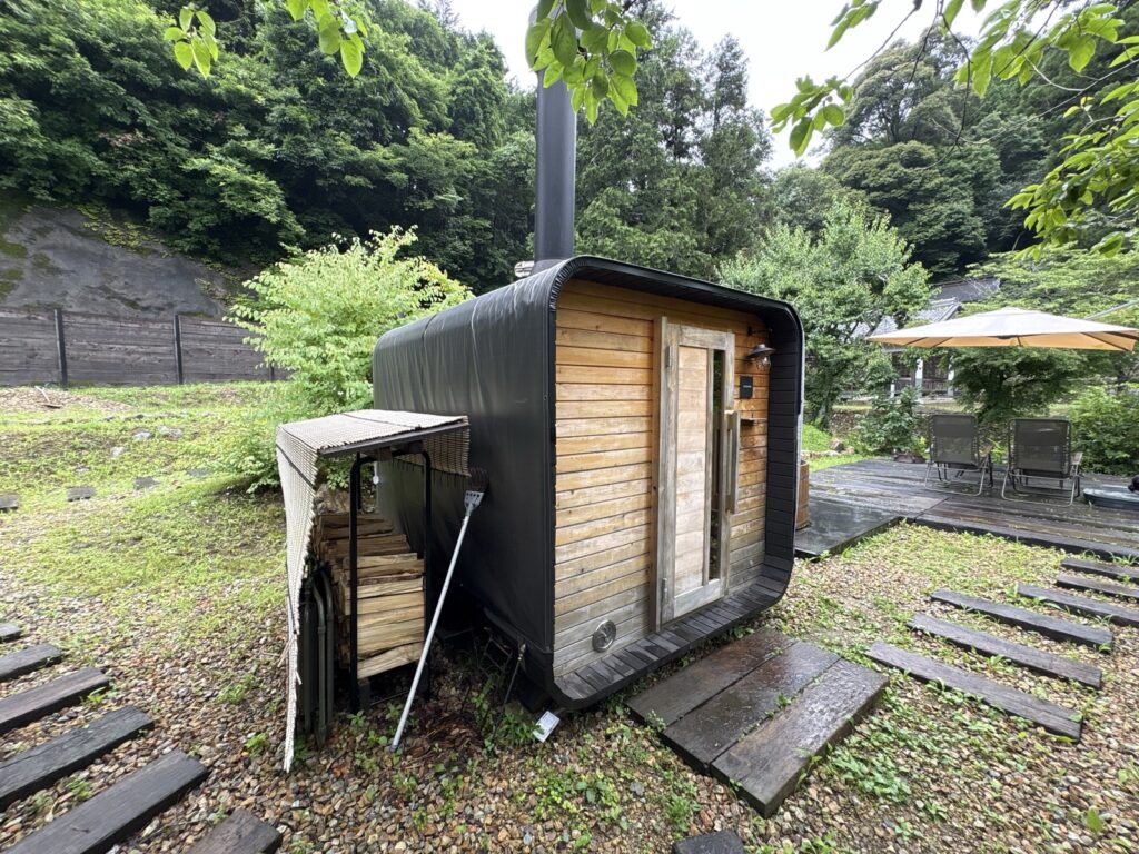 キューブサウナの外観。箱型の建物と煙突、脇に薪棚